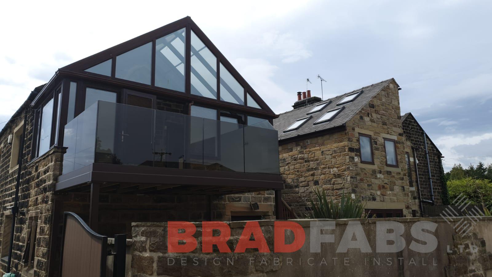 Balcony with supporting legs and bronze tinted laminated infinity glass balustrade with privacy screen to one side by Bradfabs 
