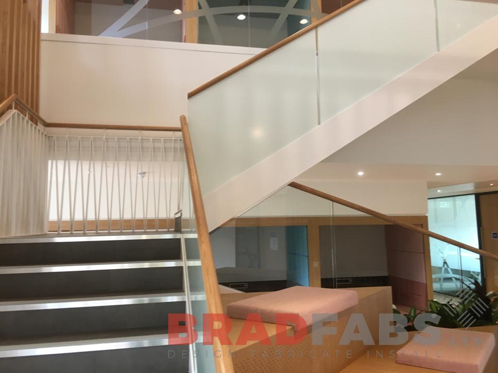 Large bespoke staircase for a commercial property by Bradfabs, decorative balustrade to one side and frosted glass balustrade to the other side, with timber handrail 
